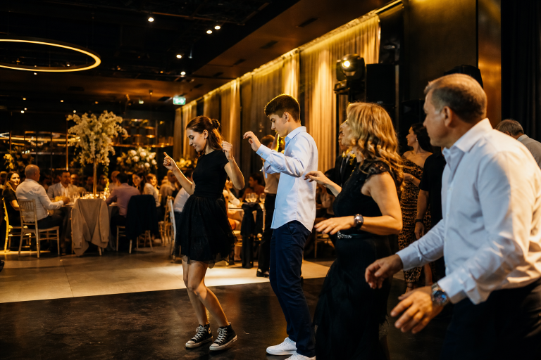 Invitați de vârste diferite încep să danseze natural, în timp ce alții socializează la mesele unui botez.