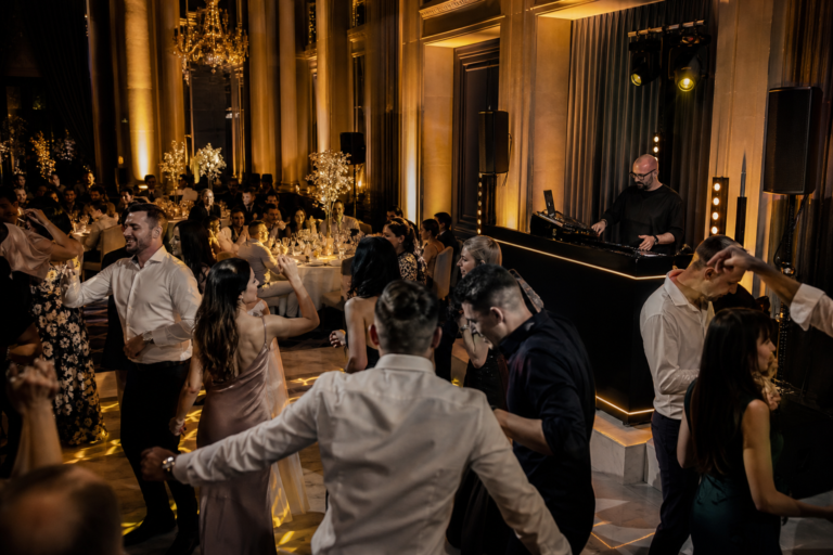Invitați care dansează într-o sală de nuntă luminată cald, cu accente discrete pe ringul de dans.