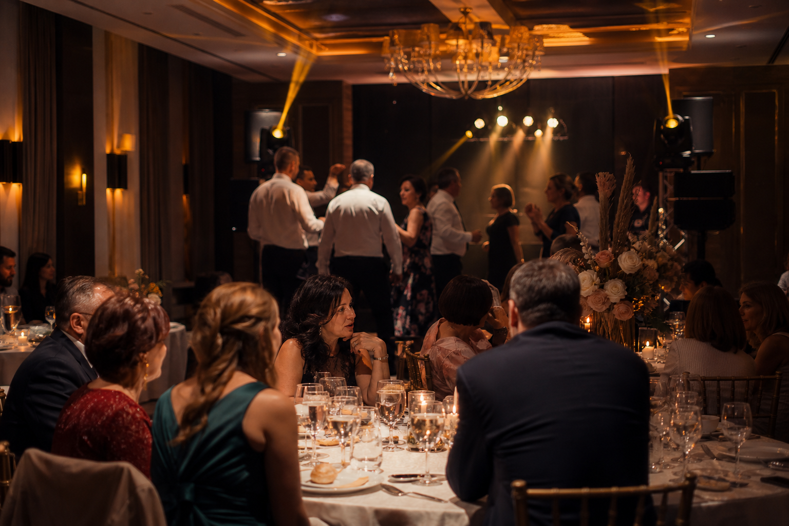 Invitați la un botez discută la mese, în timp ce alții dansează pe ring într-un salon cu sonorizare discretă.